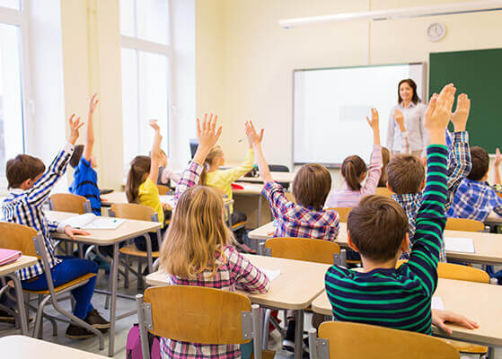 Elementary students sitting in a classroom setting with their hands raised