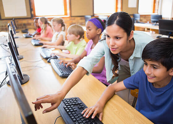 Teacher helping young students working on computers